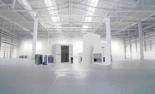 Several machines of different sizes in a huge production hall, with one person standing between them.
