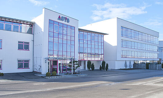 Wide view of a modern ASYS Group company building with a glass façade.