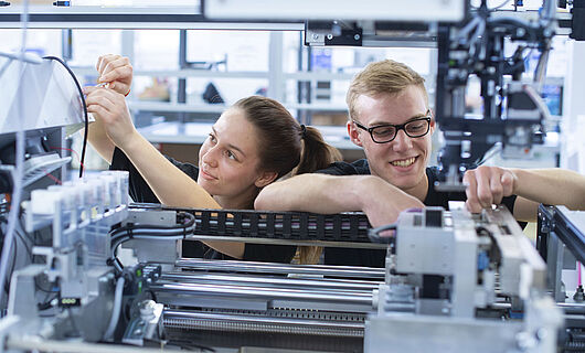 Two young people working together on the inner components of a machine.