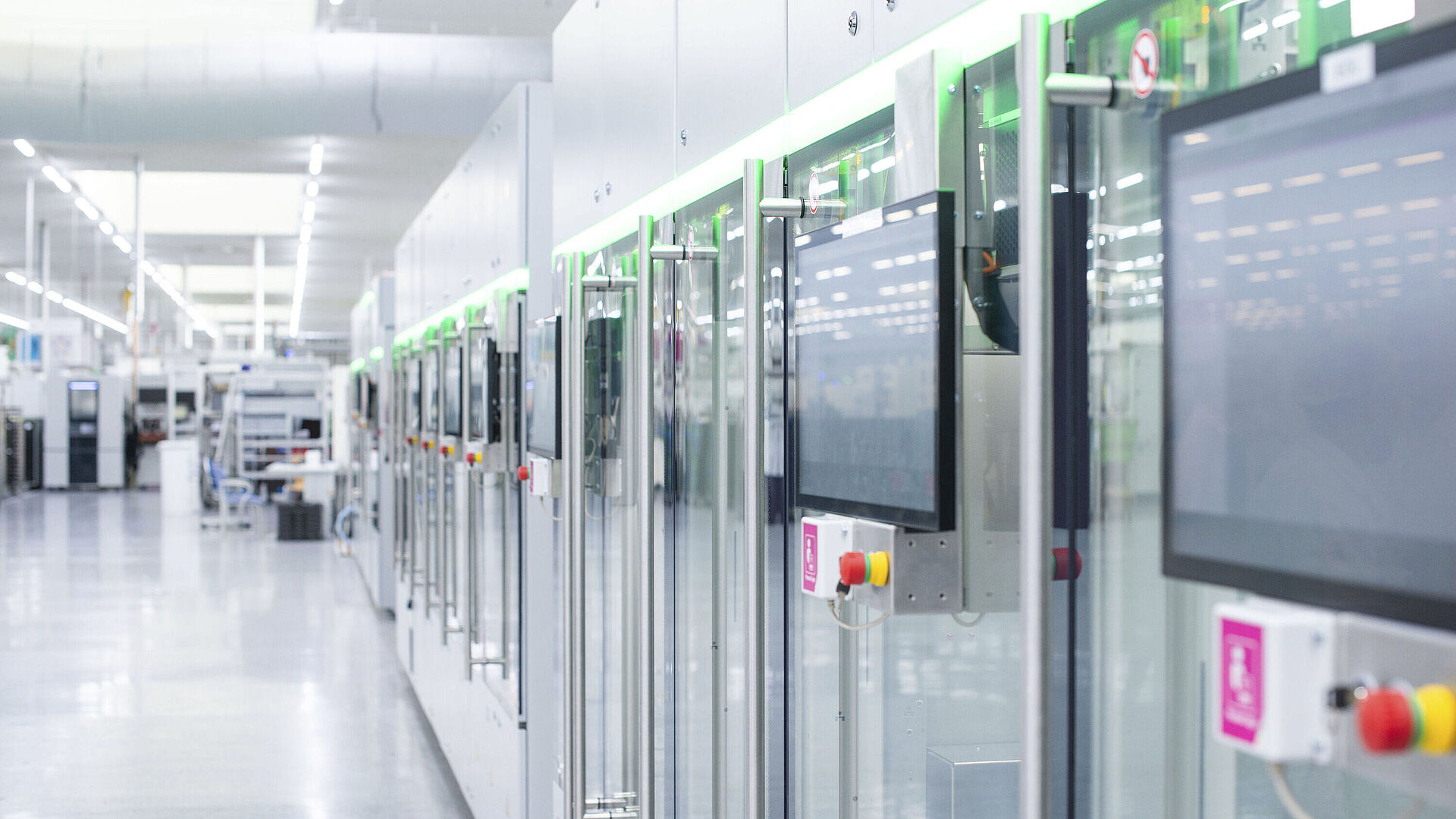 Automatisierte Fertigungslinie mit modernen Maschinen und Touchscreens in einer hellen Produktionshalle.