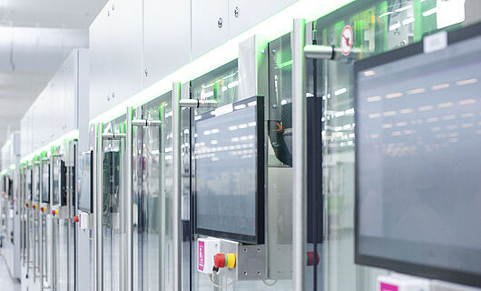 Automatisierte Fertigungslinie mit modernen Maschinen und Touchscreens in einer hellen Produktionshalle.