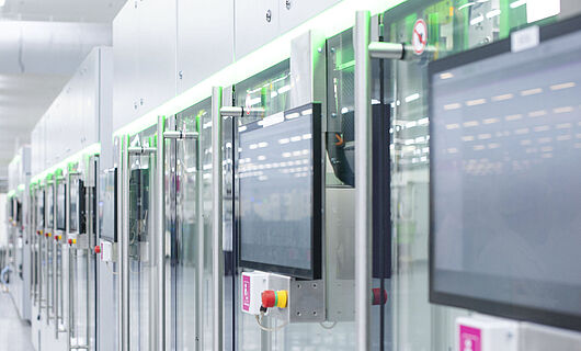Automatisierte Fertigungslinie mit modernen Maschinen und Touchscreens in einer hellen Produktionshalle.