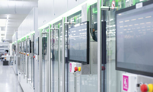 Automatisierte Fertigungslinie mit modernen Maschinen und Touchscreens in einer hellen Produktionshalle.