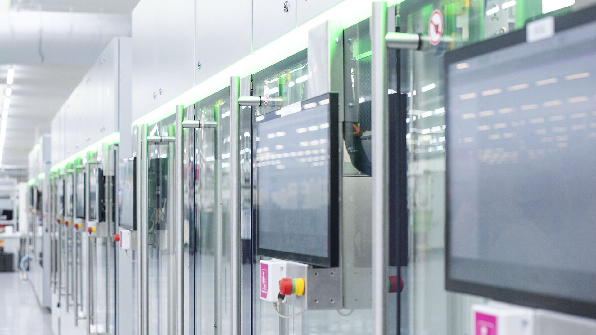 Automatisierte Fertigungslinie mit modernen Maschinen und Touchscreens in einer hellen Produktionshalle.