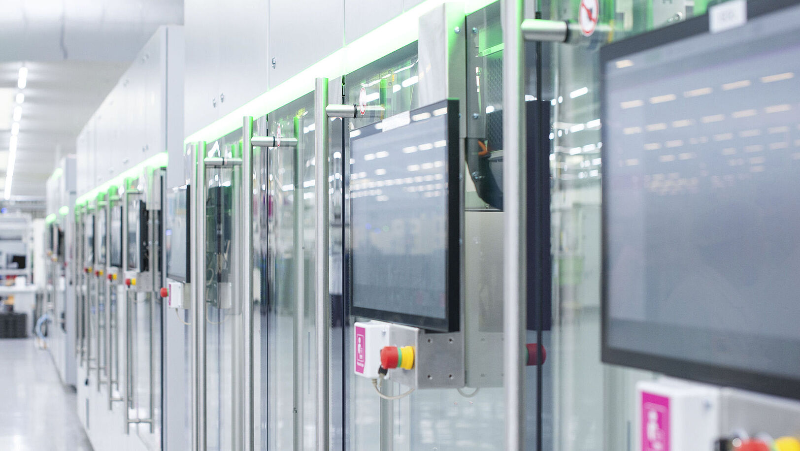 Automatisierte Fertigungslinie mit modernen Maschinen und Touchscreens in einer hellen Produktionshalle.