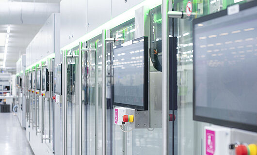 Automatisierte Fertigungslinie mit modernen Maschinen und Touchscreens in einer hellen Produktionshalle.