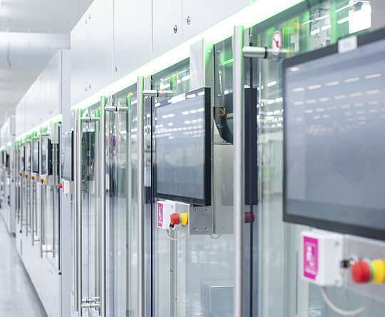 Automatisierte Fertigungslinie mit modernen Maschinen und Touchscreens in einer hellen Produktionshalle.