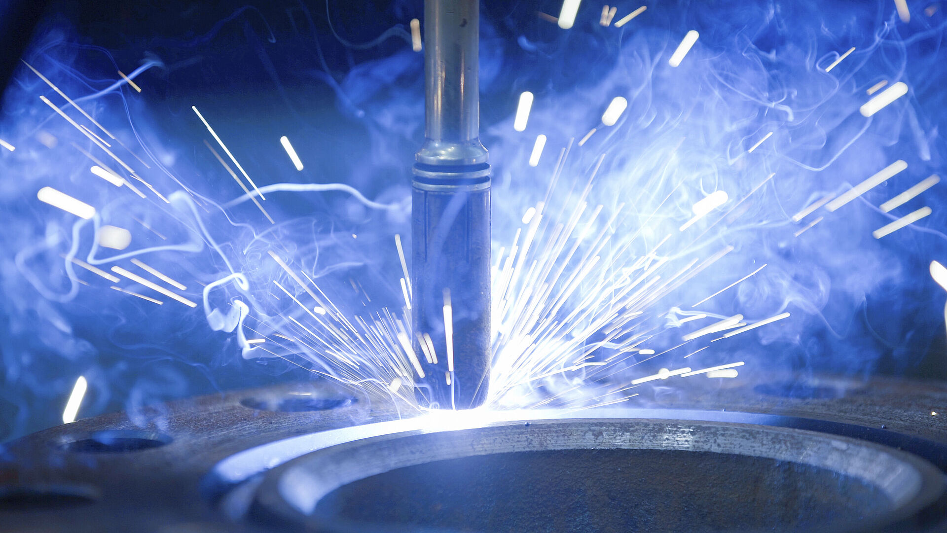 Laser welder hits a round metal object, producing many bright blue sparks.