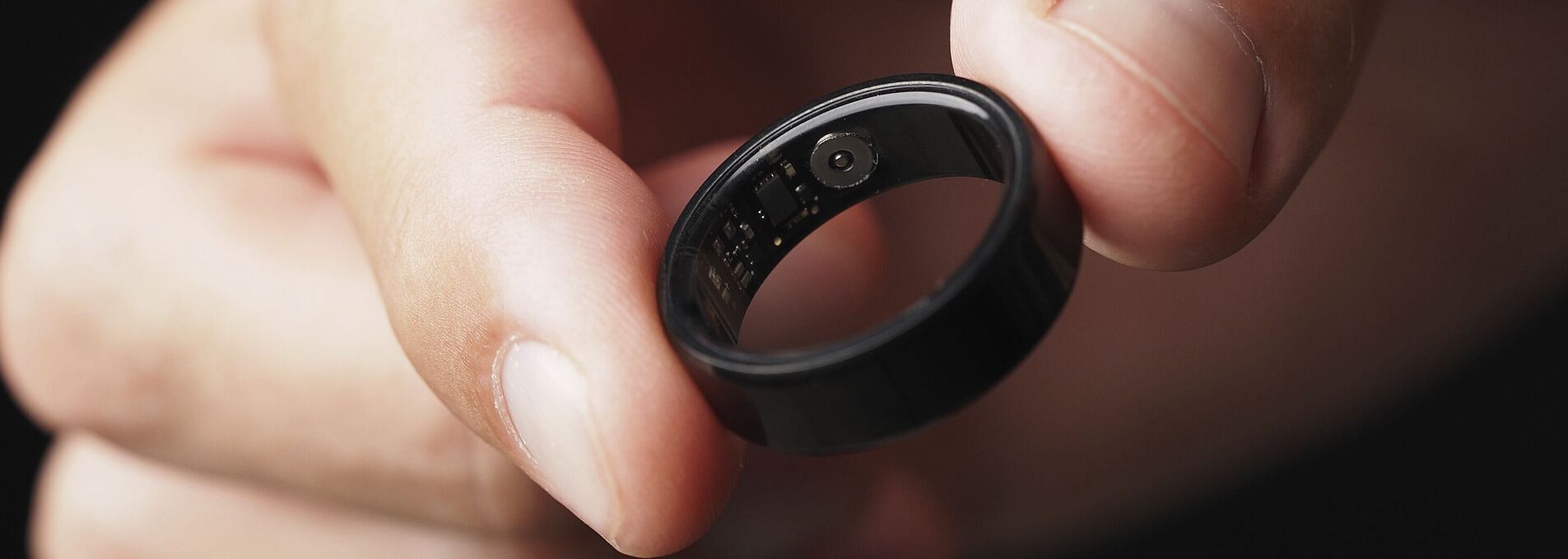 A hand holds a black smart ring between two fingers.