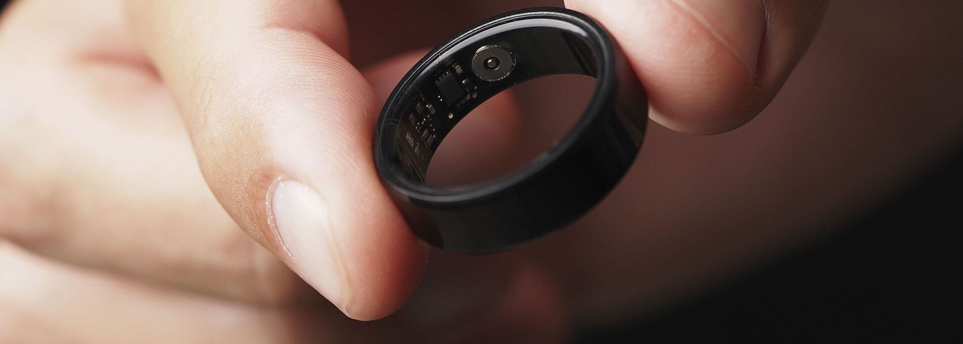 Eine Hand hält zwischen zwei Fingern einen schwarzen Smart Ring.