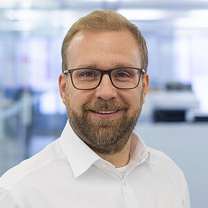 Lächelnder Mann in einem weißen Hemd. In einem gut beleuchteten Büro.