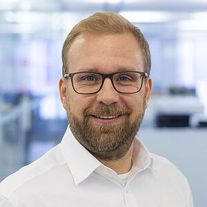 Lächelnder Mann in einem weißen Hemd. In einem gut beleuchteten Büro.
