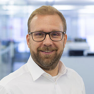 Lächelnder Mann in einem weißen Hemd. In einem gut beleuchteten Büro.