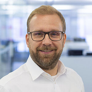 Lächelnder Mann in einem weißen Hemd. In einem gut beleuchteten Büro.