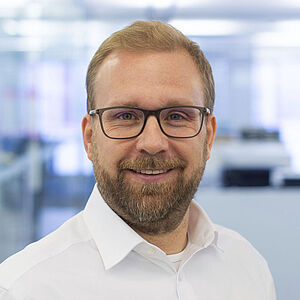 Lächelnder Mann in einem weißen Hemd. In einem gut beleuchteten Büro.