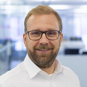 Lächelnder Mann in einem weißen Hemd. In einem gut beleuchteten Büro.