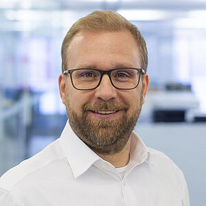 Lächelnder Mann in einem weißen Hemd. In einem gut beleuchteten Büro.