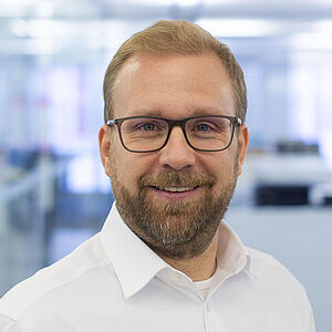 Lächelnder Mann in einem weißen Hemd. In einem gut beleuchteten Büro.