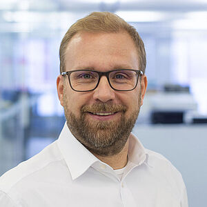 Lächelnder Mann in einem weißen Hemd. In einem gut beleuchteten Büro.