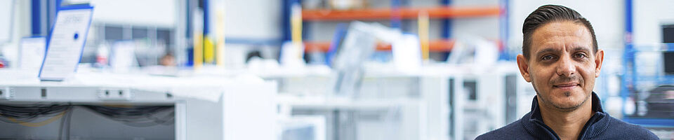 Smiling man standing in a production hall in front of several machines