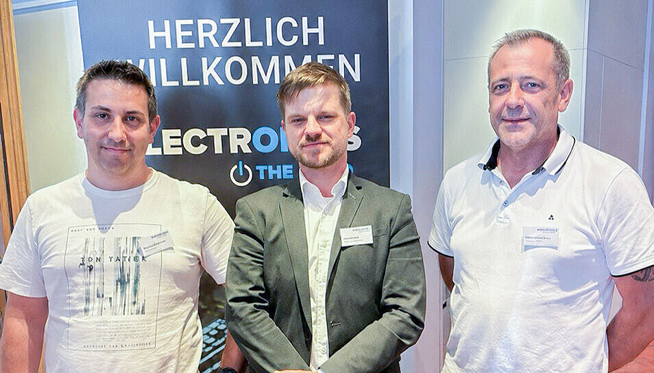 Three men are standing next to each other, smiling.