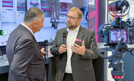 Two men in an interview in front of a running camera