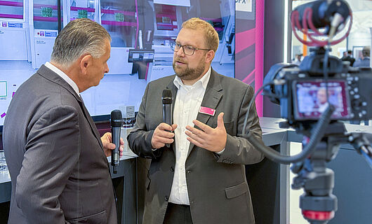 Two men in an interview in front of a running camera