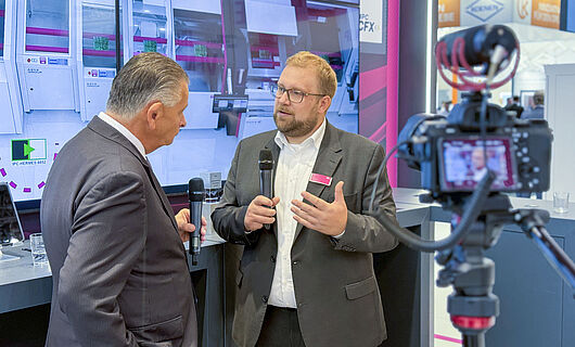 Two men in an interview in front of a running camera