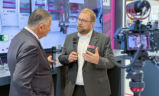 Two men in an interview in front of a running camera