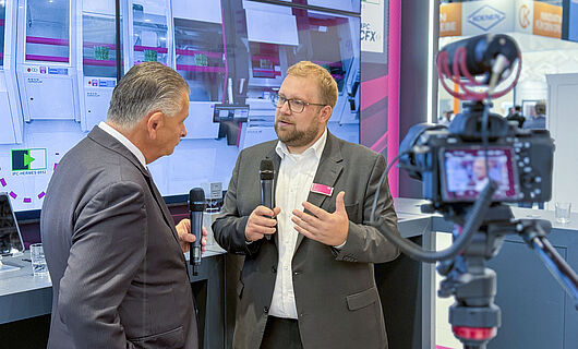 Two men in an interview in front of a running camera