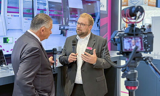 Two men in an interview in front of a running camera