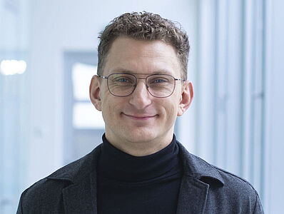 Lächelnder Mann in schwarzem Rollkragenpullover in einem gut beleuchtenden Flur.