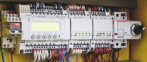 Helle Switch-Devices sind an der Wand montiert und von oben sowie unten mit zahlreichen bunten Kabeln verbunden.