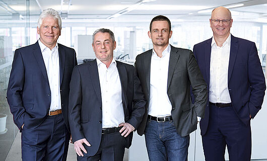Four men in suits stand next to each other and look toward the camera.