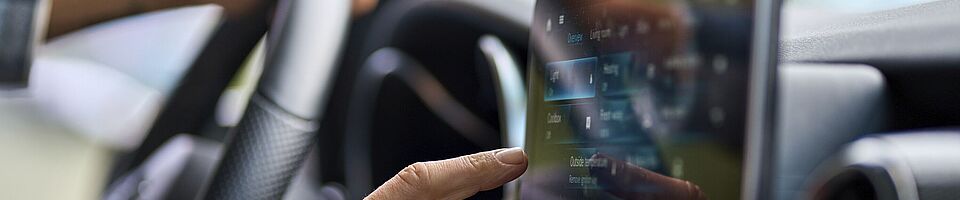 Interior of a modern car: One hand rests on the steering wheel, the other operates the central touchscreen.