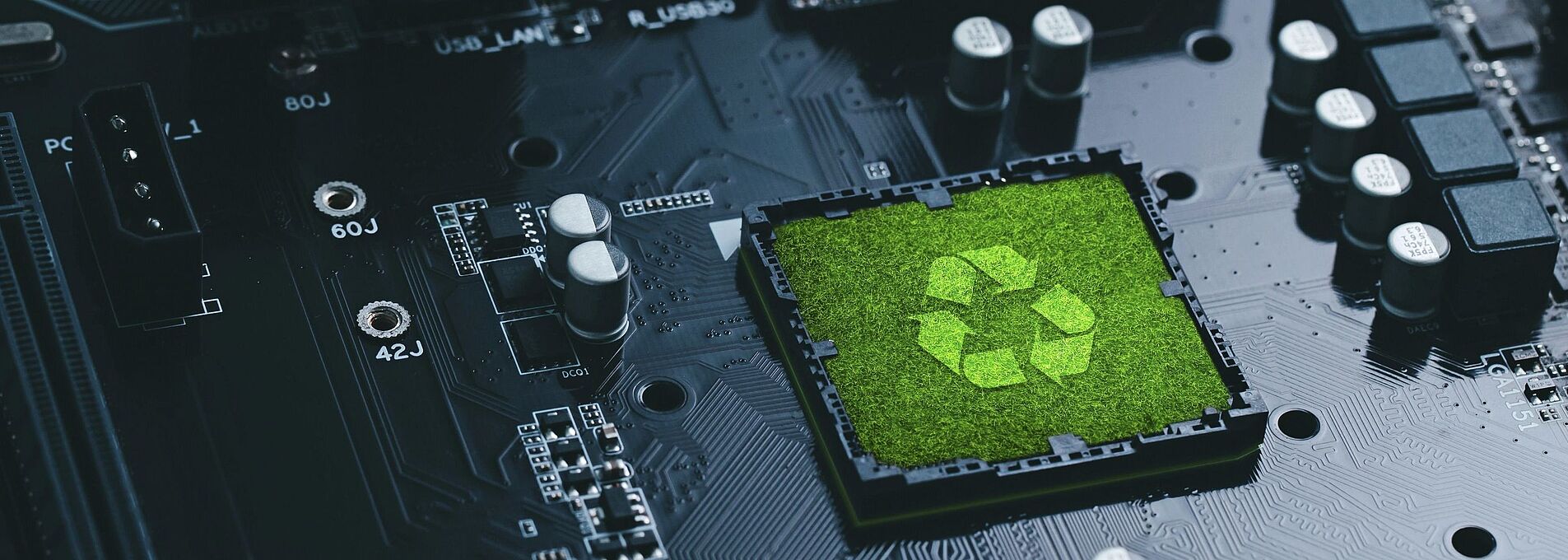 Populated circuit board with a recycling symbol on a grass field in the center.