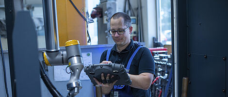 Man operates a welding robot using a control pad.