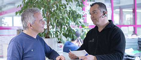 Two men are standing at a counter and looking at each other.