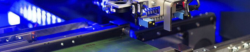 Interior view of a laser machine with an inserted circuit board. Blue light visible in the background.