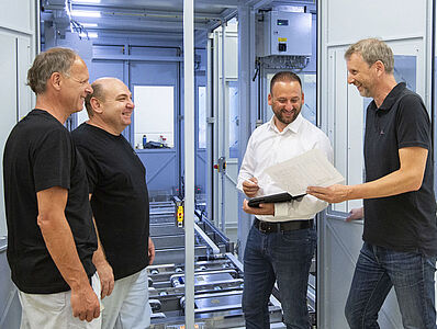 Four men are talking in front of a machine line.