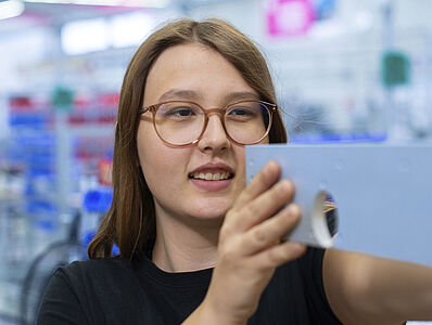 Eine junge Frau führt eine Messung in einer Produktionshalle durch.