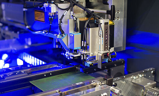 Interior view of a laser machine with an inserted circuit board. Blue light visible in the background.