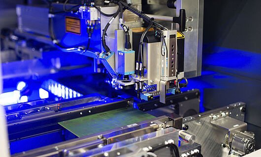 Interior view of a laser machine with an inserted circuit board. Blue light visible in the background.