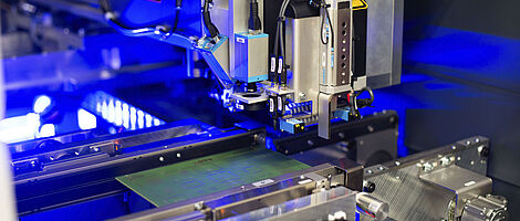 Interior view of a laser machine with an inserted circuit board. Blue light visible in the background.