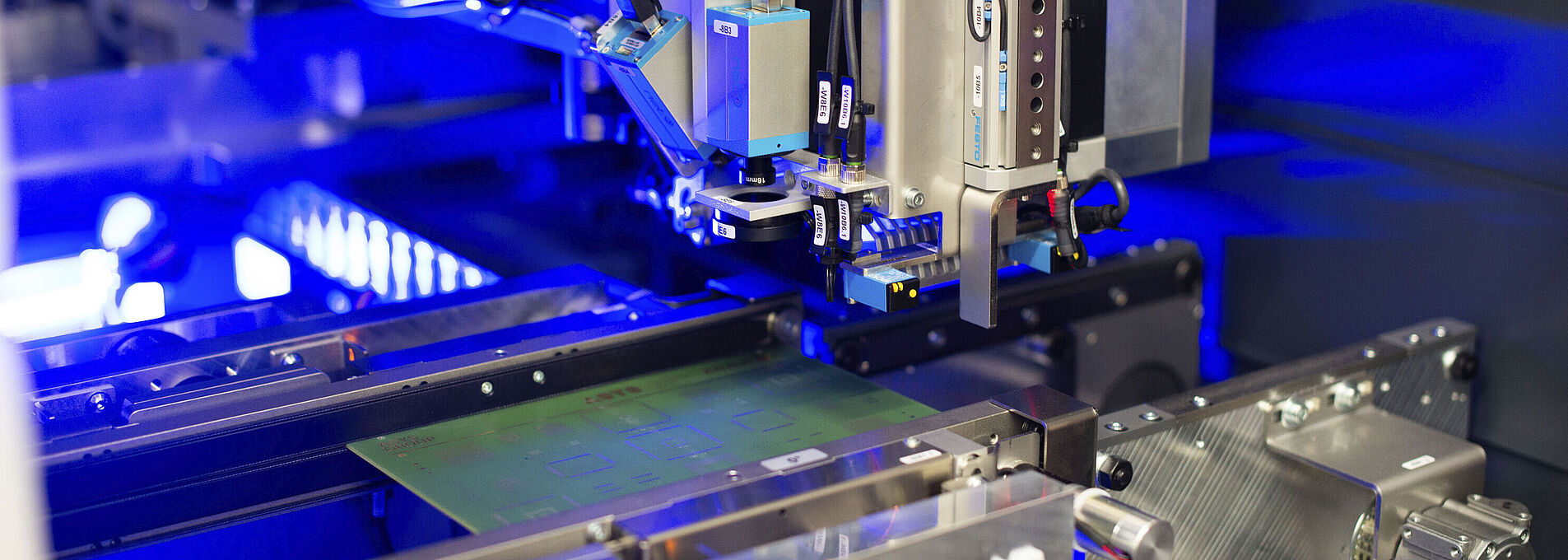 Interior view of a laser machine with an inserted circuit board. Blue light visible in the background.