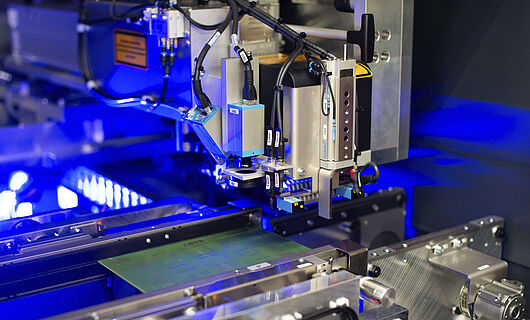 Innenansicht einer Laser Maschine mit eingelegter Leiterplatte. Blaues Licht im Hintergrund.