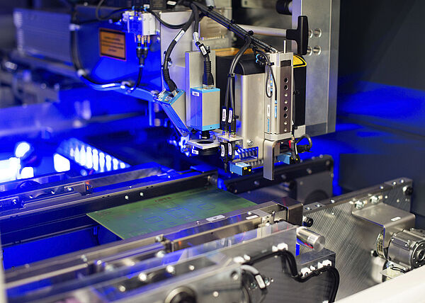 Innenansicht einer Laser Maschine mit eingelegter Leiterplatte. Blaues Licht im Hintergrund.