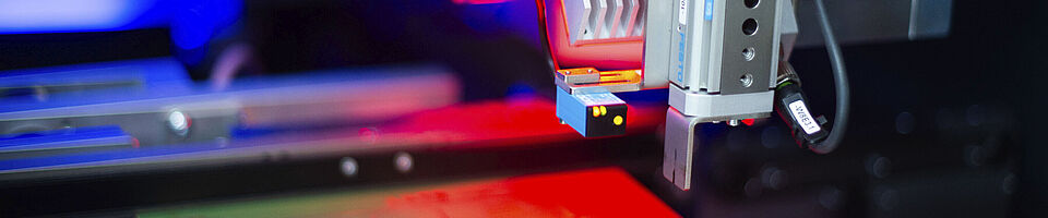 Interior view of a laser machine, red light illuminating an inserted circuit board.