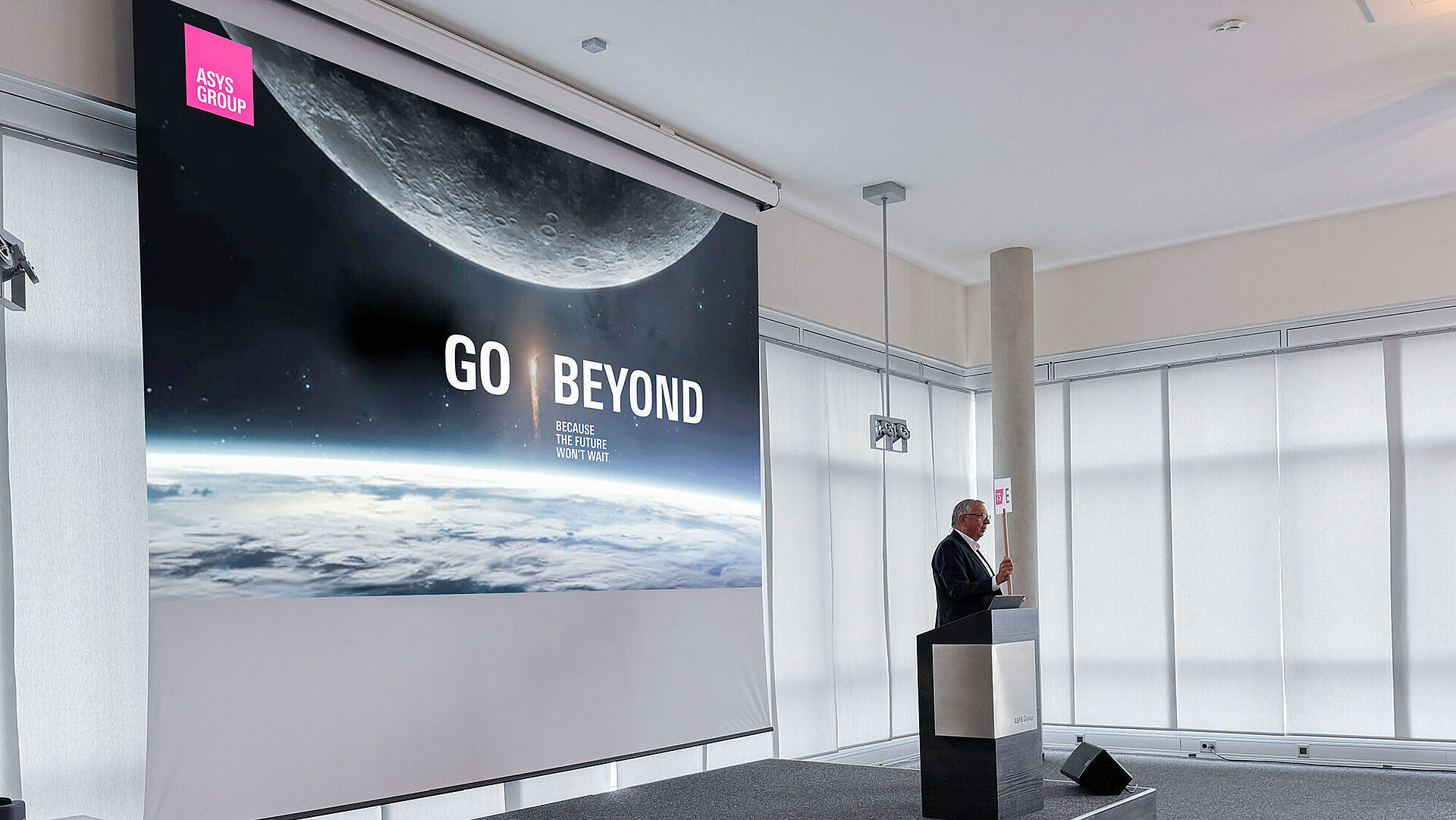 A man on a stage presenting from behind a lectern.