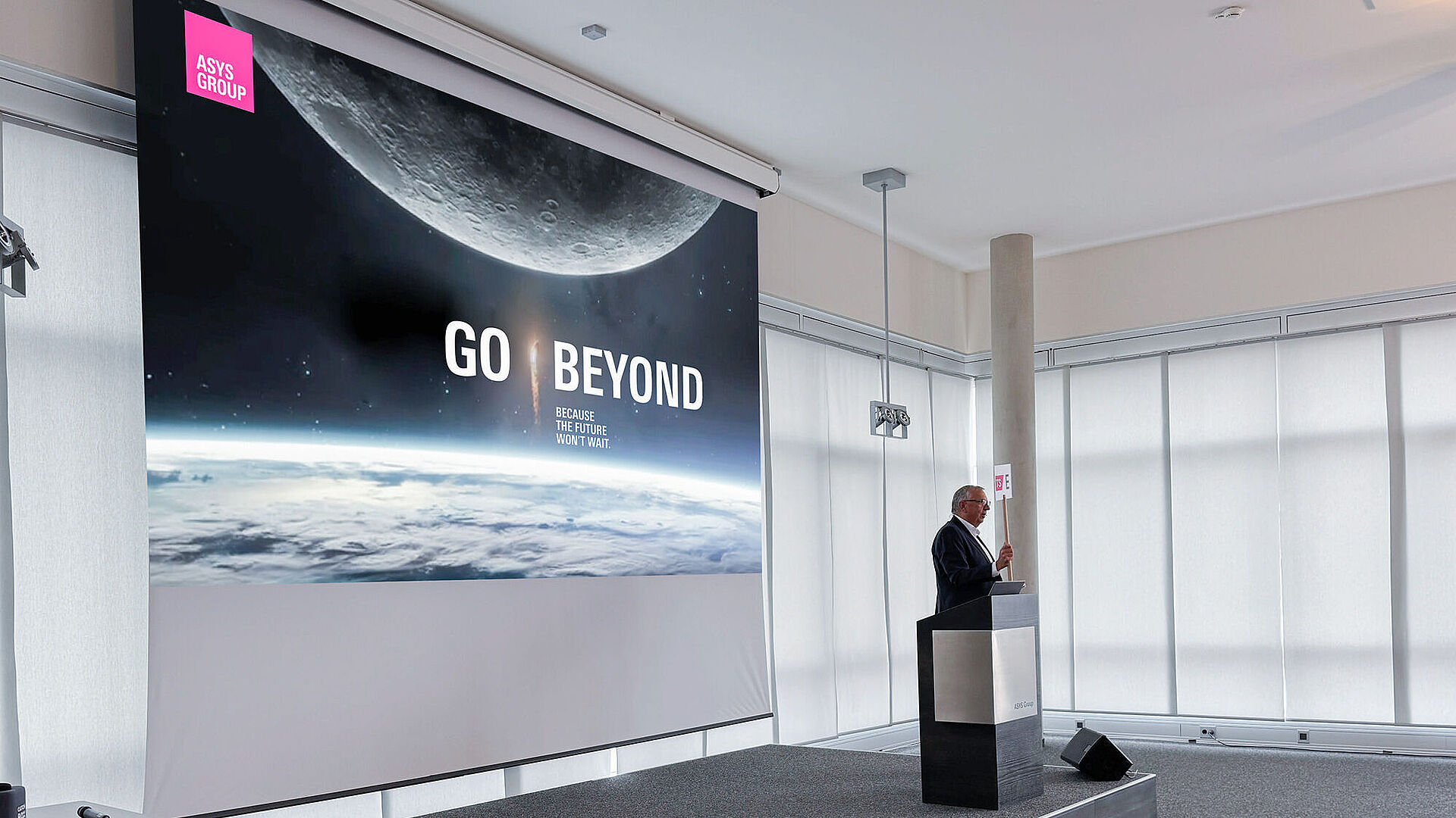 A man on a stage presenting from behind a lectern.